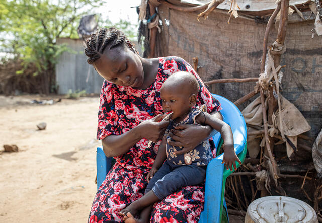 A South Sudanese mother feeds her 1-year-old daughter in her lap nutritious peanut paste at a refugee camp in Kenya.